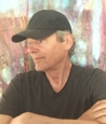 Al Van Mil wearing a black t-shirt and black baseball hat, looking off to the side.